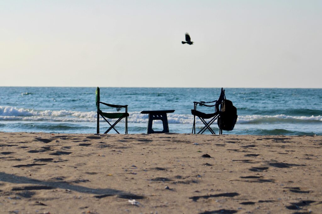 Empty beach chairs facing the serene ocean with waves breaking gently on a sunny day.
